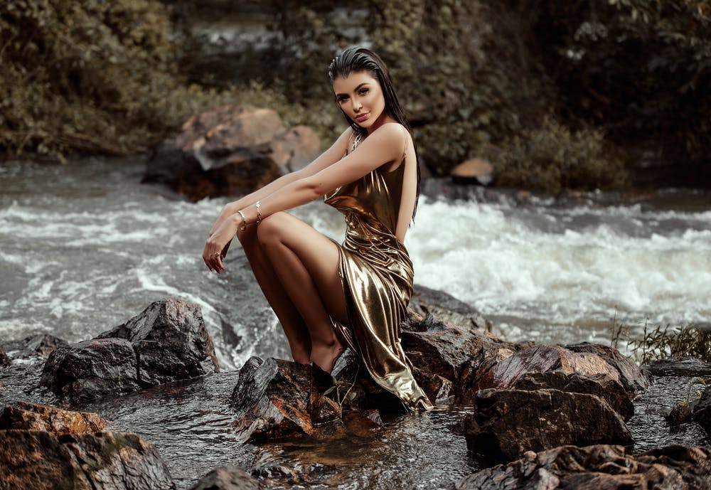 kobieta w złotej sukience siedząca na kamieniu przy rzece